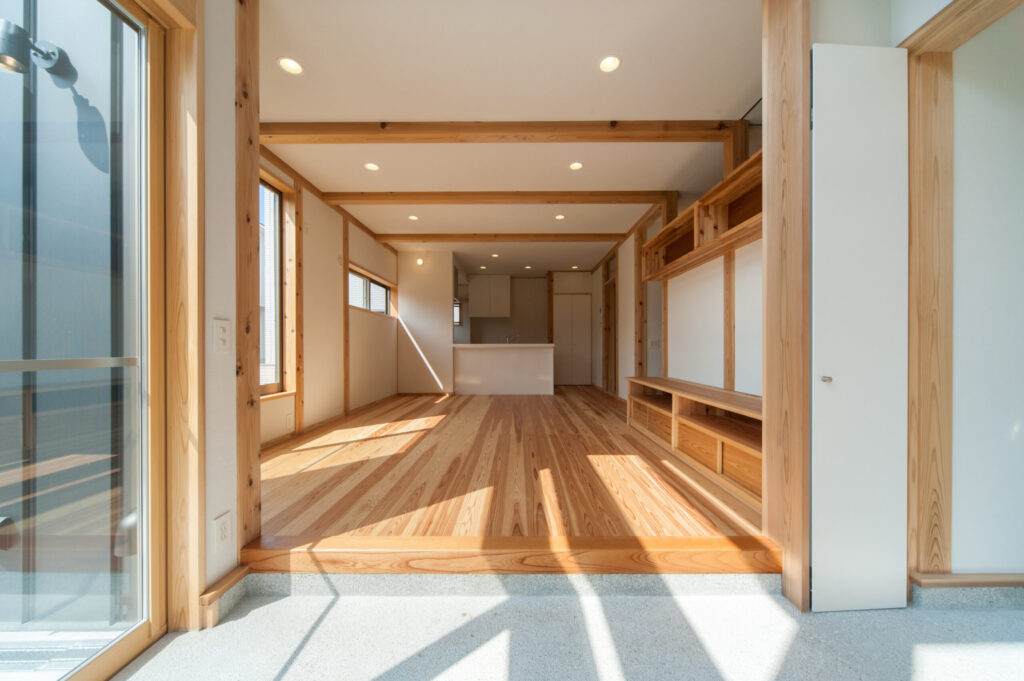 土間からつながる無垢材の床のLDK。梁をあらわした天井と造作の収納棚